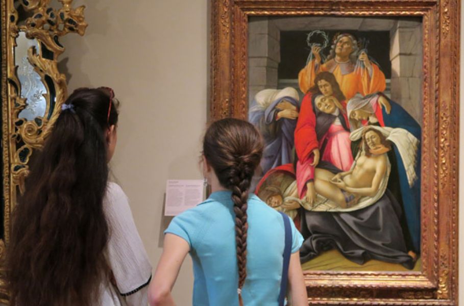 Due persone stanno osservando un dipinto rinascimentale in una cornice dorata all'interno di un museo. L'opera raffigura una scena religiosa.