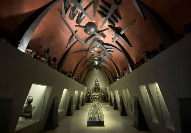 La Sala d'Armi del museo  Poldi Pezzoli con soffitto arcuato e sculture. Illuminazione calda enfatizza l'architettura e le opere esposte.