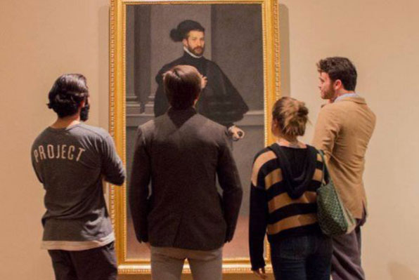 Quattro persone osservano un quadro ritraente una figura maschile in un museo. L'ambiente è tranquillo, riflessivo.