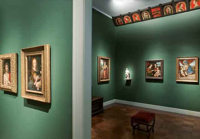La sala dei Lombardi del Poldi Pezzoli con pareti verdi e quadri d'epoca appesi. Una piccola panca in legno si trova al centro.