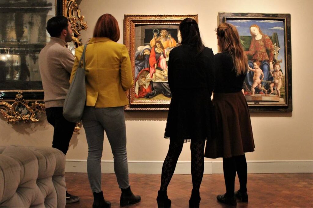 Quattro persone osservano opere d'arte tra cui il compianto Compianto sul Cristo morto di Botticelli