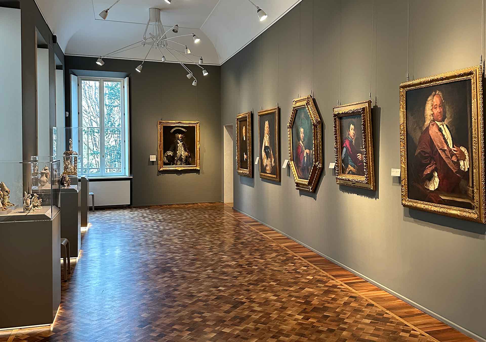Galleria dei Ritratti del Museo Poldi Pezzoli con pareti grigie, quadri appesi e vetrine con oggetti esposti, illuminazione naturale da finestra.