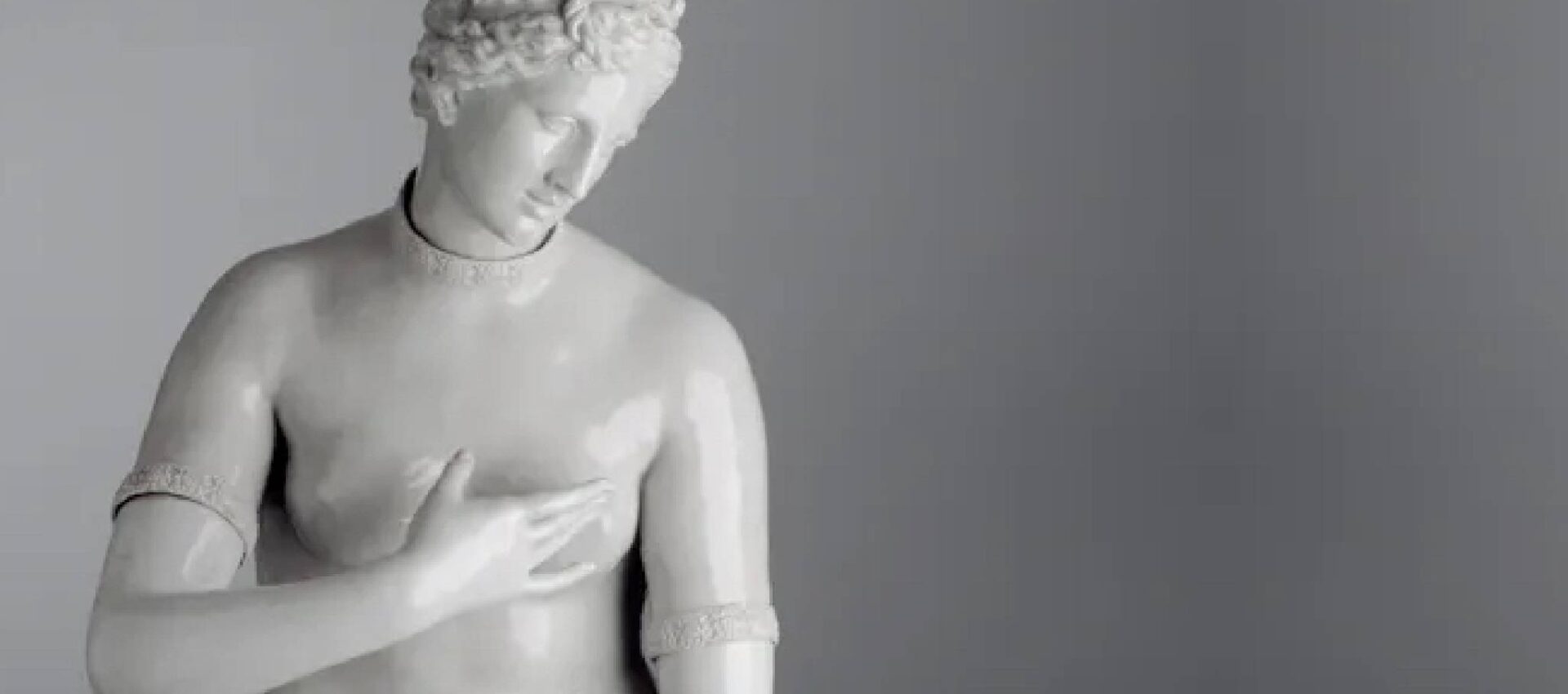 Venere de' Medici manifattura Ginori di Doccia, scultura in porcellana bianca raffigurante una figura classica con lo sguardo basso, mano sul petto, capelli ricci, tratti somatici definiti, sfondo neutro.
