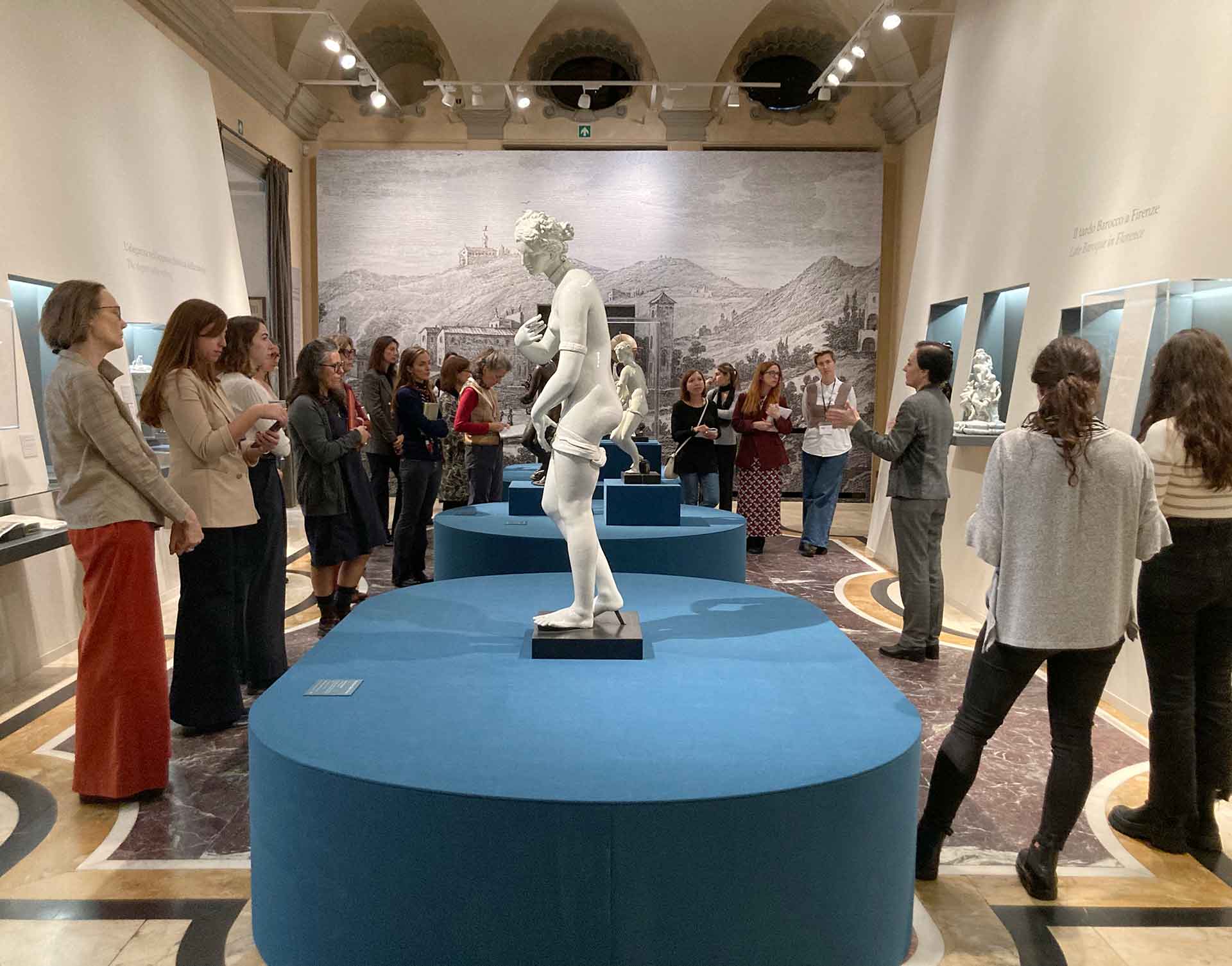 Un gruppo di persone osserva una statua in occasione della mostra Oro Bianco al Museo Poldi Pezzoli. Ambiente elegante con decorazioni murali, pavimenti colorati e illuminate artificialmente.