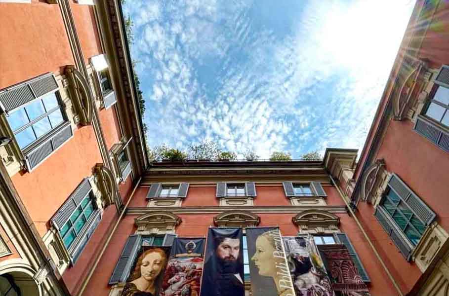 Un'inquadratura dal basso dell'dificio del Museo Poldi Pezzoli con banner appesi alla facciata. Il cielo è azzurro con nuvole bianche sparse.
