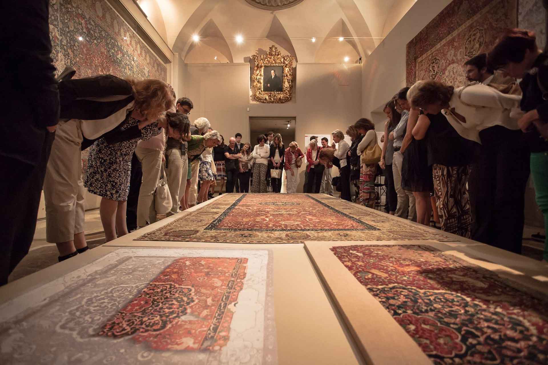 Un gruppo di persone osserva attentamente antichi tappeti esposti nella sala dell'affresco del museo poldi pezzoli.