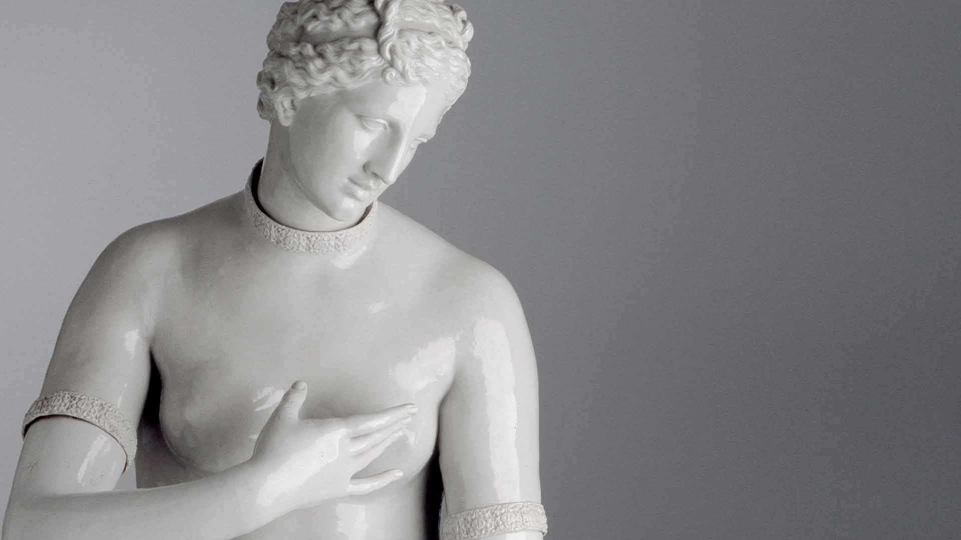 Venere de' Medici manifattura Ginori di Doccia, scultura in porcellana bianca raffigurante una figura classica con lo sguardo basso, mano sul petto, capelli ricci, tratti somatici definiti, sfondo neutro.