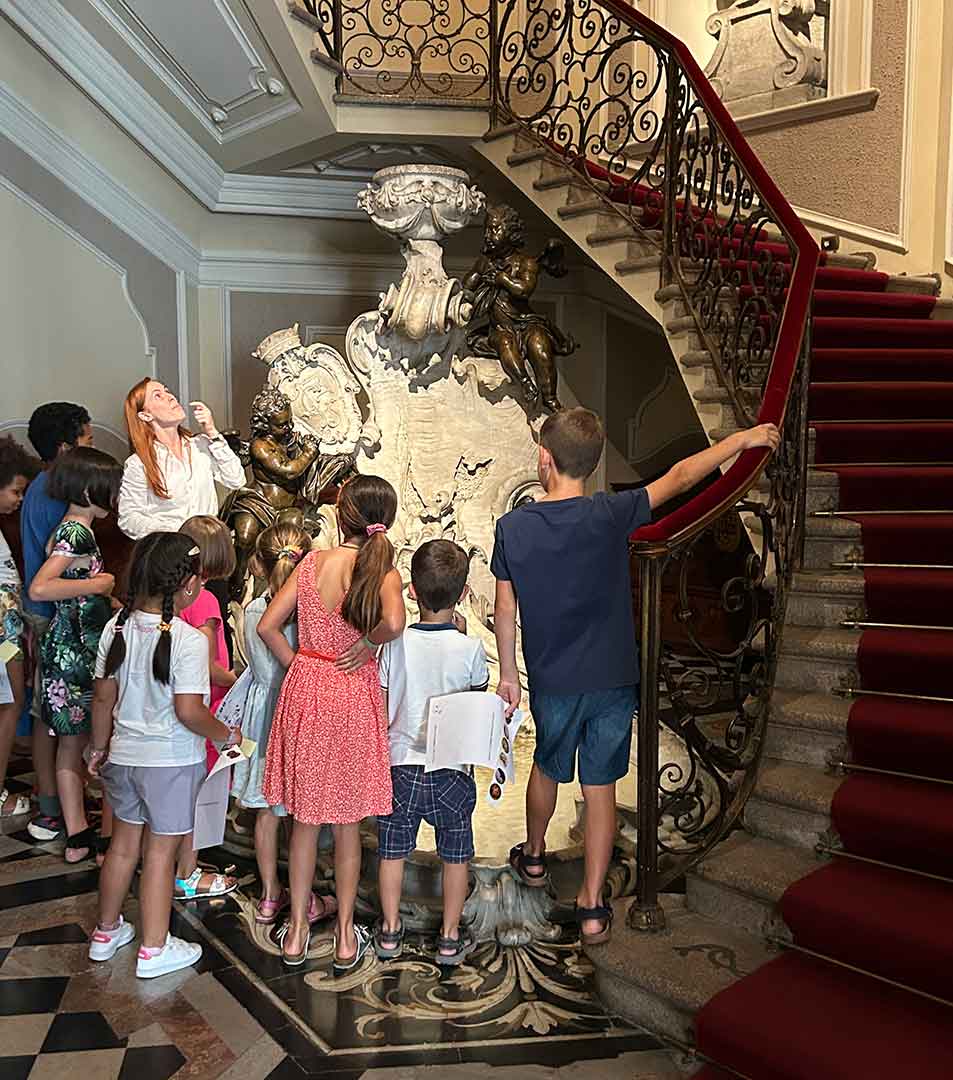 Un gruppo di bambini e un adulto osservano una statua nello Scalone Antico del Museo Poldi Pezzoli.