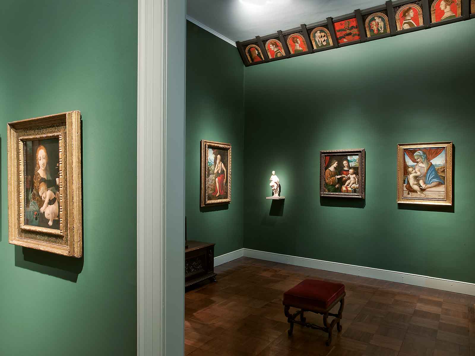 Le Sale dei Lombardi del Museo Poldi Pezzoli con pareti verdi e opere d'arte. Quadri appesi e una scultura su una colonna illuminata. 
