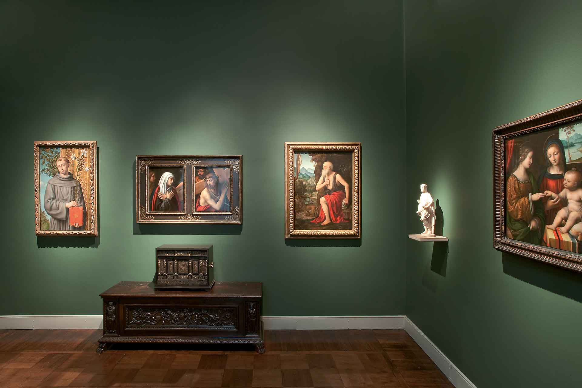 La sala dei Lombardi con pareti verdi e pavimento in legno. Quadri appesi, una scultura e un cofanetto antico su un mobile scuro.