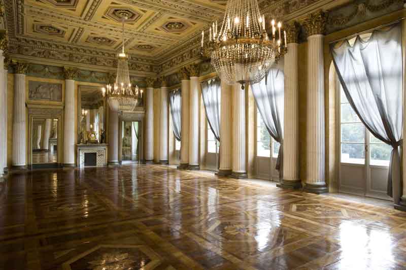 Una sontuosa sala con decorazioni della Galleria d’Arte Moderna di Milano, soffitto dettagliato, lampadari di cristallo, grandi finestre con tende e un caminetto elegante, riflettendo opulenza e storia.