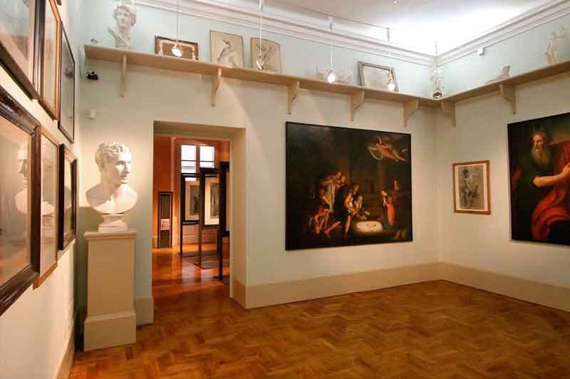 Questa immagine mostra una sala del Museo Diotti a Casalmaggiore con pavimenti in legno e pareti con quadri e sculture. L'illuminazione è calda.