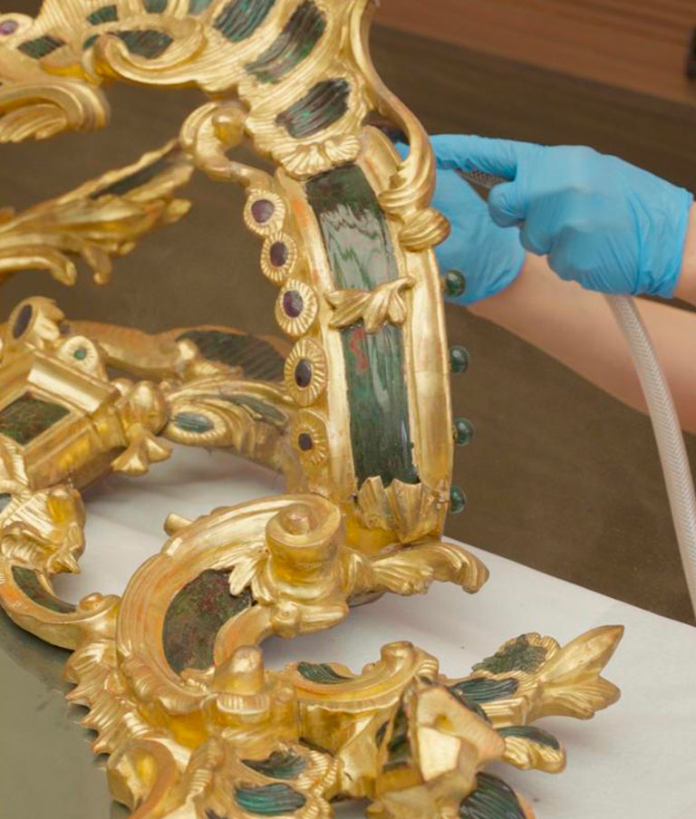 Dettaglio della cornice dorata durante la pulitura: gli inserti in vetro verde incorniciati da piccoli tondi, alcuni scheggiati dal tempo