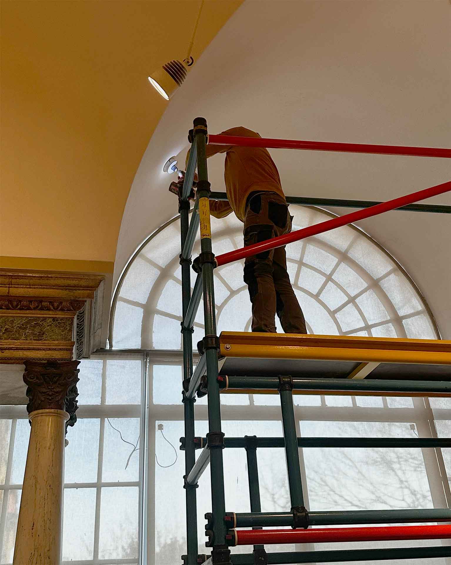 Milano, 2025. Un tecnico ispeziona lo spazio dietro il controsoffitto del Salone Dorato: sotto l'impalcatura, il capitello e la colonna marmorea della serliana, ancora nascosti